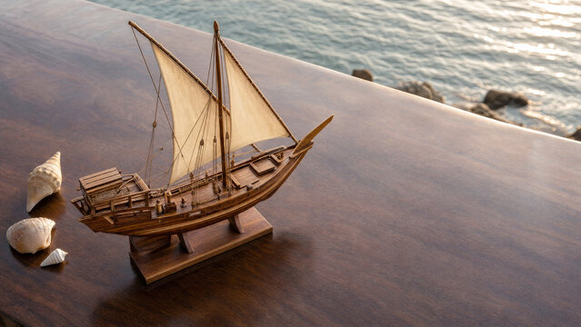 Wooden dhow model on polished surface with coastal light and seashell accents.