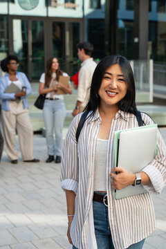 Asian female University student smiling at camera standing in front college entrance