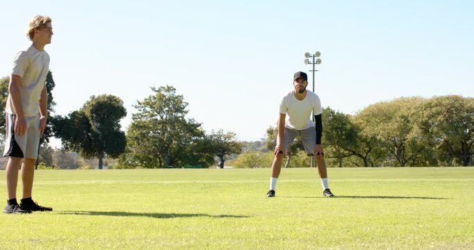 Diverse teammates holding defensive stance on grass field, with black cap, compression sleeve