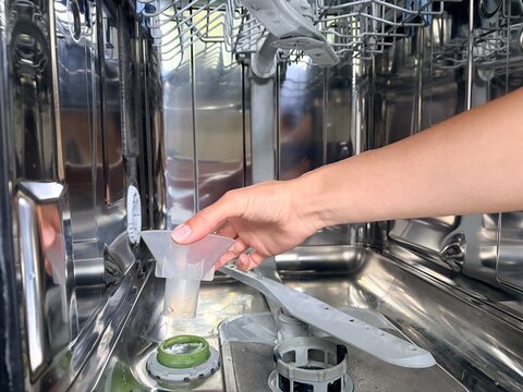 A photo of a woman's hand inserting a funnel inside a dishwasher to refill the salt supply.