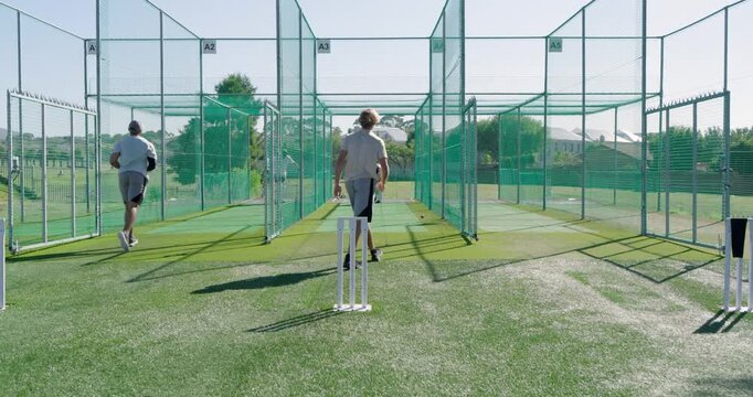 Training diverse male teammates bowling and batting in outdoor net lanes, stumps and gloves