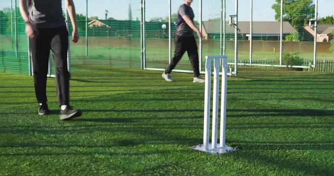 Hand gesture sparking male teammates alternating ball throws at net and pickups by stumps