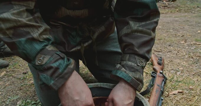 German soldier holding rifle cartridge above helmet liner in forest