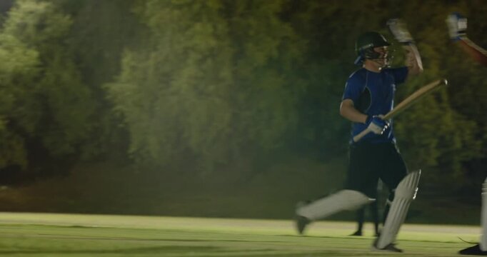 Male batsman reacting to bowler delivering ball, driving shot sprinting with floodlights