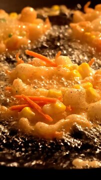 Vegetable fritters with corn and carrots frying in hot bubbling oil for traditional Asian cuisine