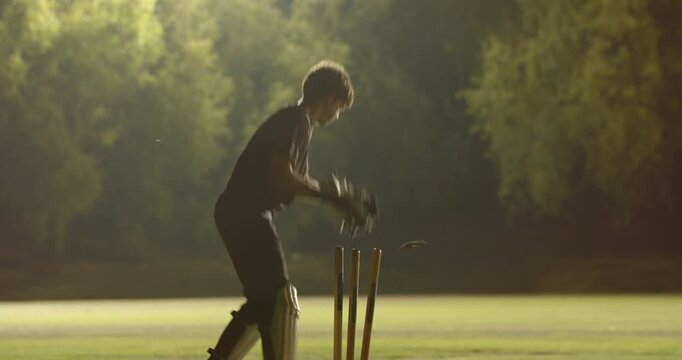 Male wicketkeeper catching ball after yorker, breaking stumps for wicket under floodlights