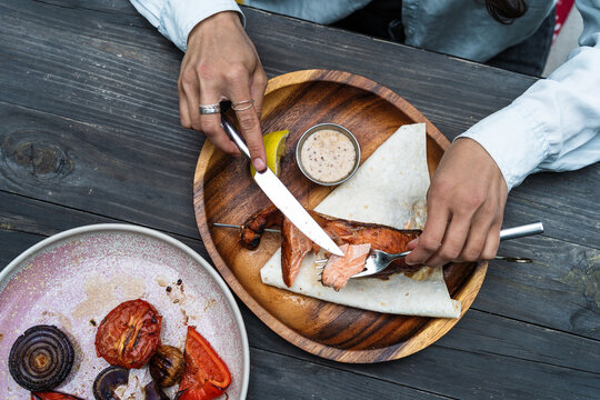 High angle view of unrecognizable person cutting grilled salmon steak with knife and fork