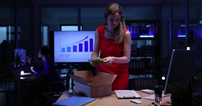 Businesswoman gathers stuff into cardboard box leaving workplace. Woman manager quits job in commercial company in evening. Reduction of team