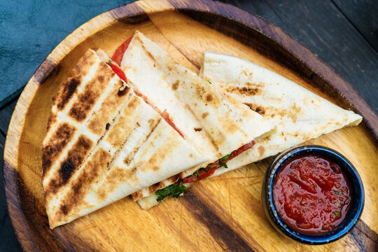 High angle view of crispy Mexican quesadillas served with tomato salsa sauce on a wooden plate