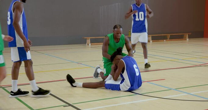 Defender causing fall, african american player dribbling basketball in gym, huddling to help