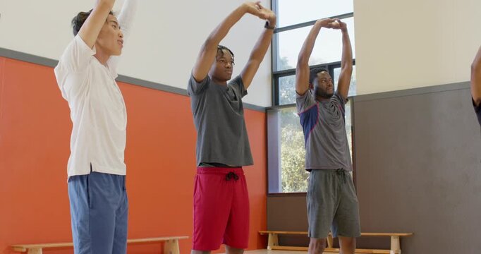 Three men raising arms overhead in gym with red wall, fourth man crossing behind in tracker