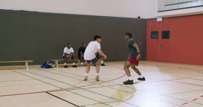 Asian man dribbling crossover while man sliding defense snatching basketball for gym drill