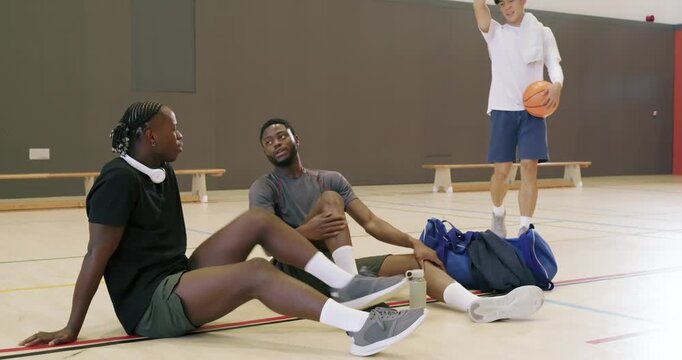 Dribbling asian athlete entering gym making diverse male friends smile while sitting