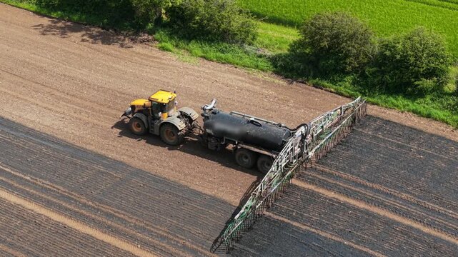 Commercial farming machinery applying slurry manure fertilizer for agricultural soil enrichment. Field nutrient replenishment supporting agribusiness productivity, fertility restoration, sustainable