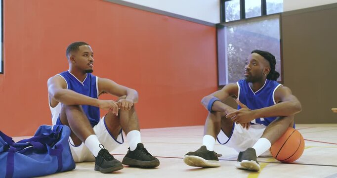 Settling onto court postgame, african american teammates talking about game, ball under leg