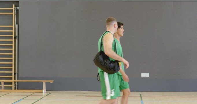 Entering gym court two players with duffel bag and bottle walking then fist bumping huddling