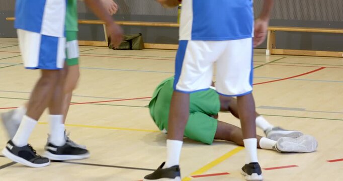 Stealing ball male defender knocking attacker down at gym, male teammate assisting knee