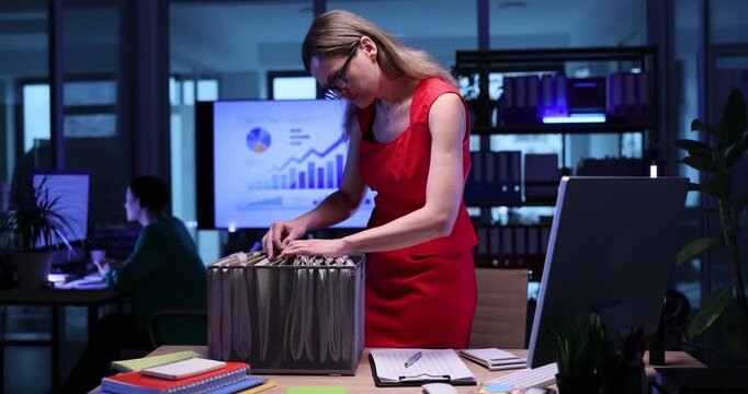Nervous woman manager seeks files on rack in semi-dark office. Female employee in glasses exhausted by paperwork stays overtime in company workplace