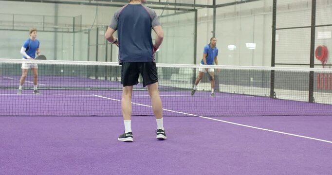 Diverse male padel players returning ball volley by swinging paddle on padel court