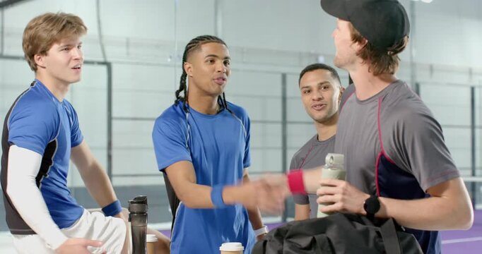 Diverse male teammates studying on phone by sideline bench and greeting returning player