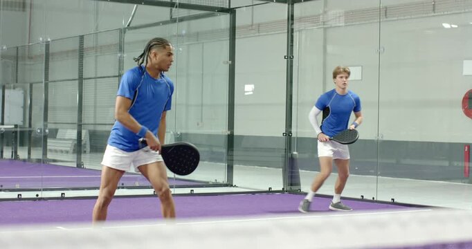 male teammates watching ball coming volleying on paddle court then sharing hug