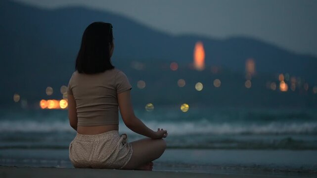 Woman meditating on beach shoreline with sea waves and Lady Buddha in Da Nang, Female practicing mindfulness by ocean at sunset with coastal mountains 4k