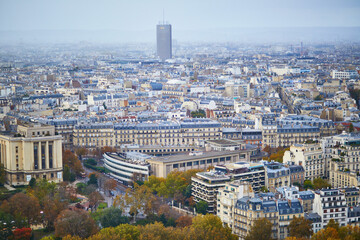Fototapeta premium View of Paris from the Eiffel Tower with autumn trees, historic rooftops, dense urban architecture, and Montparnasse Tower