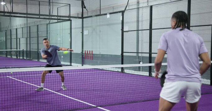 Diverse male athletes serving ball and smashing overhead with rackets rallying at court