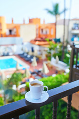 Obraz premium Cup of coffee on a hotel balcony overlooking a swimming pool and tropical courtyard in Tenerife, Canary Islands, Spain.
