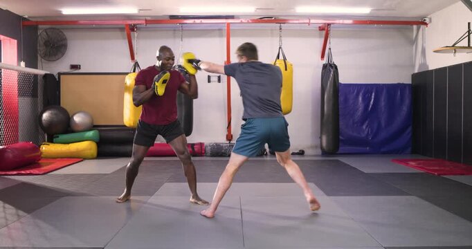 Trainer shifting focus mitts signalling punches as trainee wearing gloves punching for training