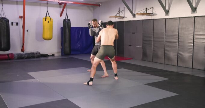 Diverse male fighters entering gym with boxing gloves exchanging strikes and takedown drills