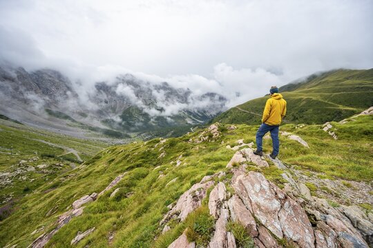 Mountaineer with yellow jacket looking at mountain landscape, cloudy rocky mountain peaks Wolayer K&ouml;pf and Biegenk&ouml;pfe, Carnic Alps, Carnic High Trail, Carinthia, Austria