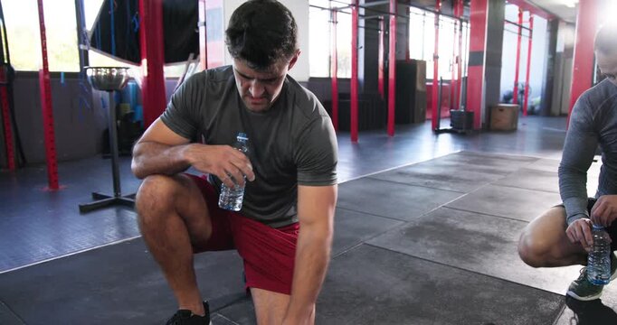 Diverse male workout duo hydrating from water bottles before performing dumbbell rows on gym