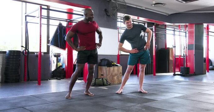 Diverse male duo leaning left mirroring side bends and hugging knees for balance high-fiving