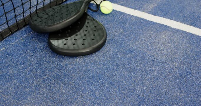 Camera tilting upward revealing two padel rackets resting on court beside black net for match