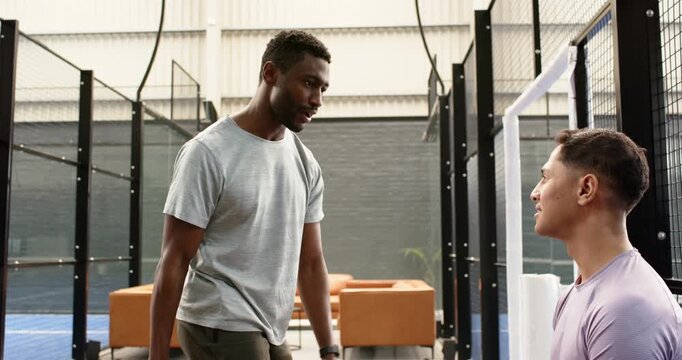Holding racket, african american coach showing grip, swing teaching male player on padel court