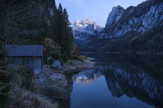 The Vordere Gosausee lake in autumn with a view of the Dachstein mountain range. The Gosaukamm on the right. Good weather, blue sky. In the evening, after sunset. Reflection. A small wooden hut on the left. Vorderer Gosausee, Gosau, Gosau valley, Salzkammergut, Upper Austria, Austria