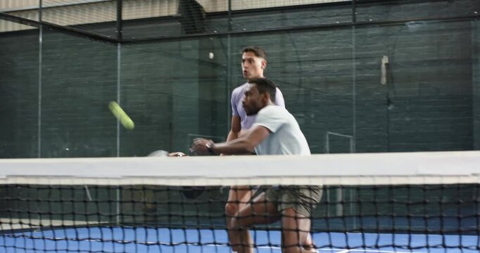 Diverse male teammates in sportswear reacting to ball volleying backhand and smashing on court