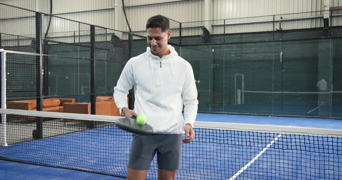 Man stepping onto blue court behind net bouncing ball with padel racket improving control