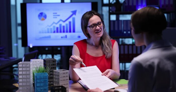 Smiling woman real estate agent offers contract to lady customer in office. Female manager sells commercial building to partner in successful agency