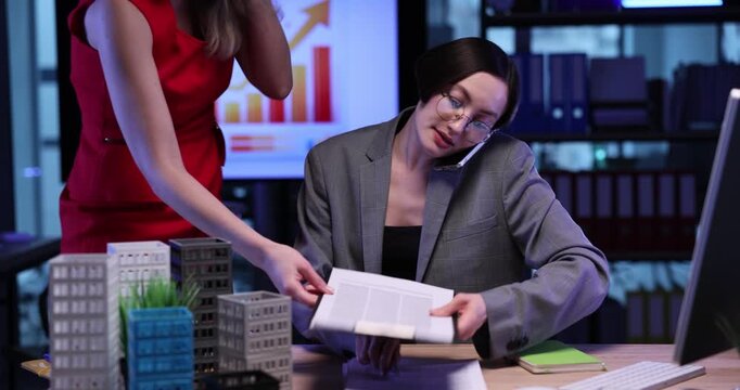 Busy real estate agent talks on mobile phone and signs papers in office. Female manager consults client on call as assistant brings contract documents