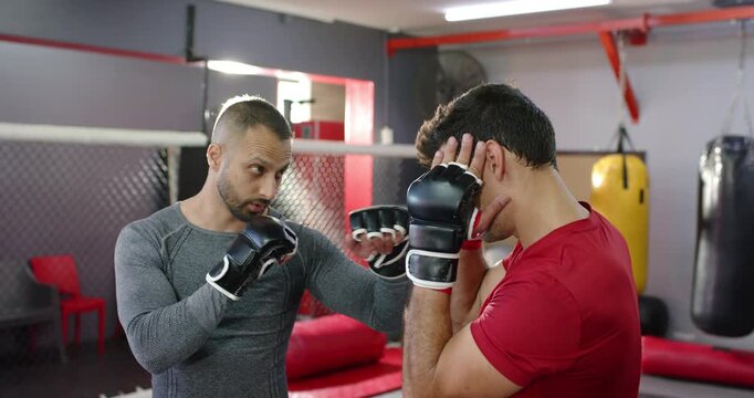 Diverse trainer and trainee throwing jabs, increasing pace, adjusting guard in gym wearing gloves