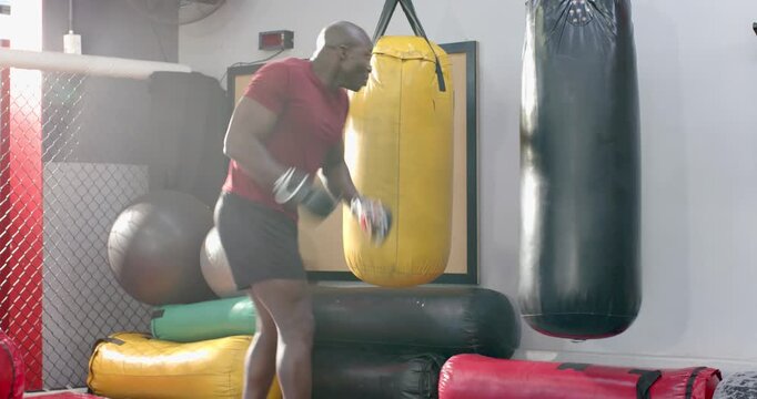 African American man bouncing, executing flying kick delivering strikes to bag at gym for drill