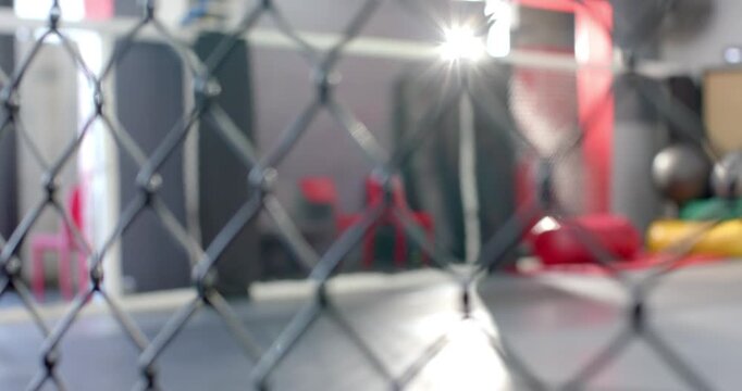 Camera is pulling focus from chain-link fence to reveal mats and hanging bags for martial arts