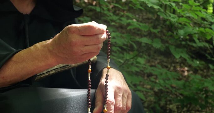 Close up of a monk's hands with rosary beads during prayer or religious practice in the forest.