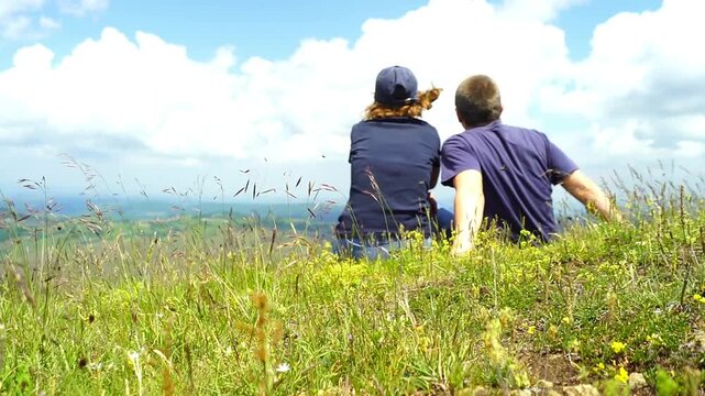 Hikers settle among alpine vegetation and share quiet pause overlooking mountain valley. Illustrates shared contemplation and the quiet intimacy of two people pausing together in highland wilderness.
