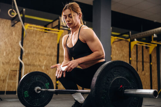 Female weightlifter in black sportswear prepares to lift a barbell with weights in a gym setting, focused on her technique and form during training