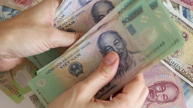 Close up view of hands counting stack of Vietnamese dong paper money bills in Vietnam. Concept of financial accounting, wealth, business budget calculation, domestic cash expenses and income tax.