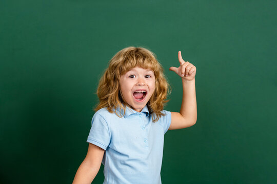 Schoolboy standing near blackboard with an idea. Funny little boy pointing up on blackboard. Back to school. Copy space