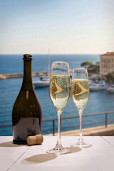Obraz premium Champagne flutes and bottle on balcony overlooking seaside marina. Concept of luxury travel, celebration toast, romantic riviera getaway, premium sparkling wine and coastal resort leisure.